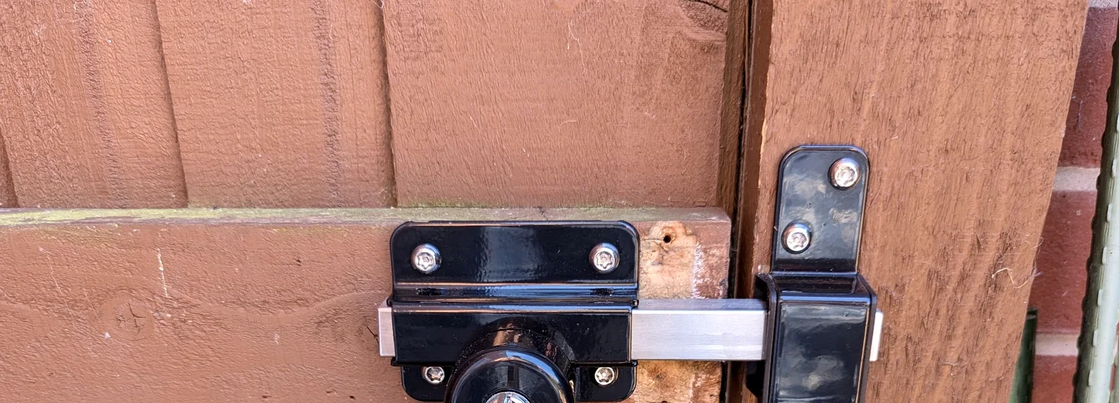 Black outdoor gate lock fitted to a brown timber gate