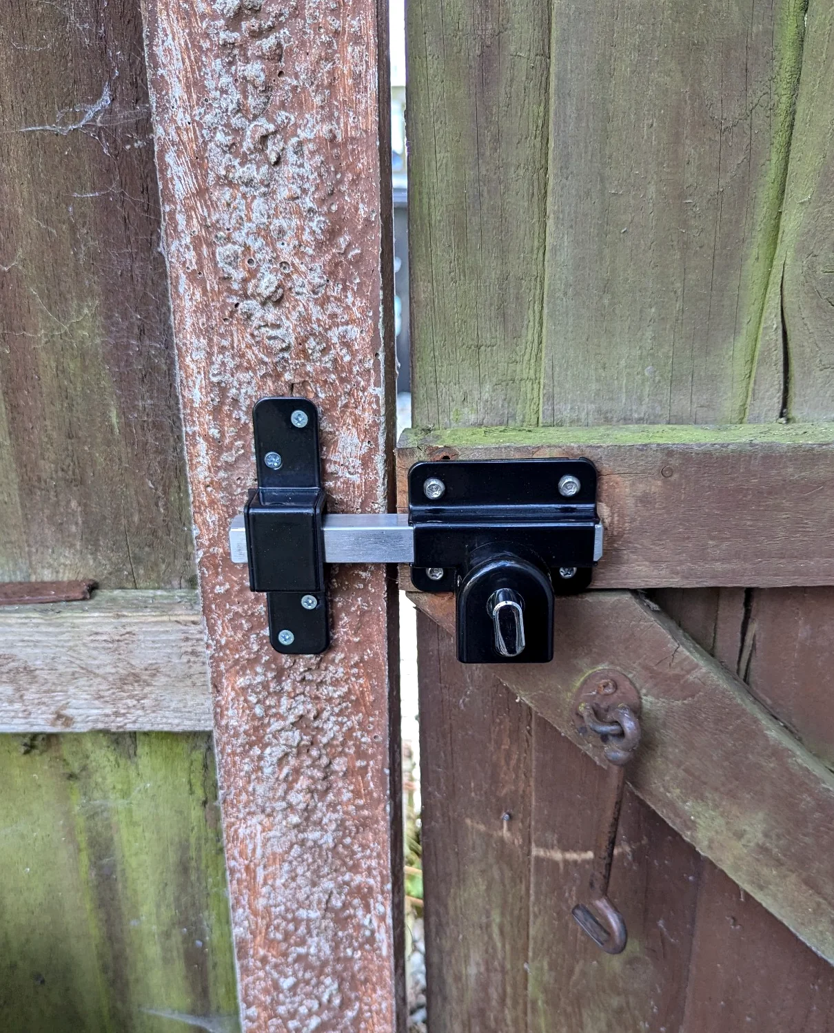 Black outdoor gate lock fitted on a green timber gate